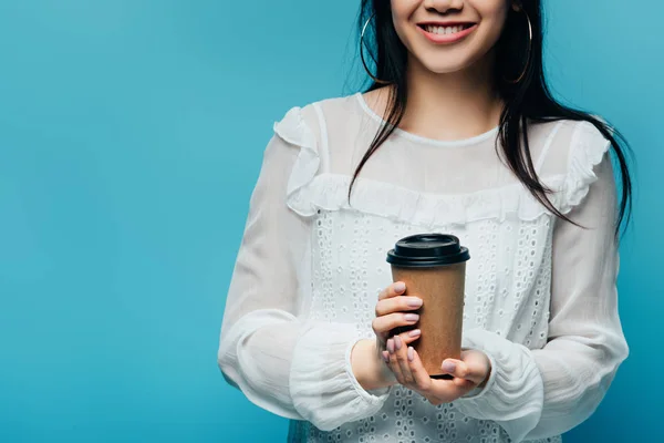 Cropped view of smiling brunette asian woman holding coffee to go on blue background — Stock Photo