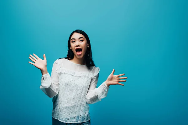 Excité brunette asiatique femme avec bouche ouverte sur fond bleu — Photo de stock