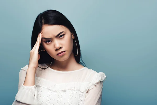 Upset brunette asian woman with headache on blue background — Stock Photo