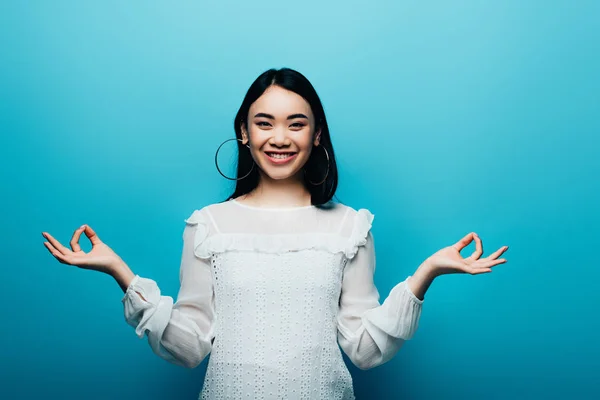 Happy brunette asian woman meditating on blue background — Stock Photo