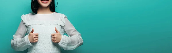 Обрізаний вид щасливої брюнетки азіатська жінка, показує великі пальці на бірюзовому фоні, панорамний знімок — стокове фото