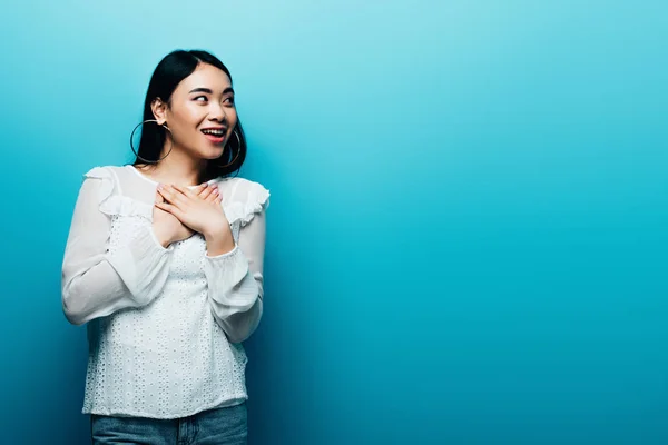 Happy shocked brunette asian woman looking away on blue background — Stock Photo
