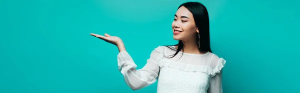 Щаслива брюнетка азіатська жінка на бірюзовому фоні, панорамний знімок — стокове фото