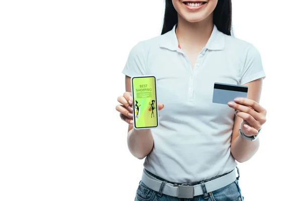 Vista ritagliata di sorridente bruna ragazza asiatica in possesso di carta di credito e smartphone con la migliore app di shopping isolato su bianco — Foto stock