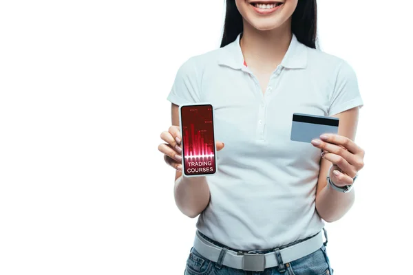 Cropped view of smiling brunette asian girl holding credit card and smartphone with trading courses app isolated on white — Stock Photo