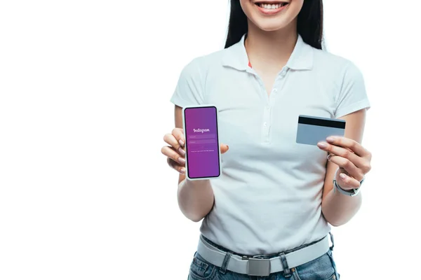 KYIV, UKRAINE - JULY 15, 2019: cropped view of smiling brunette asian girl holding credit card and smartphone with Instagram app isolated on white — Stock Photo