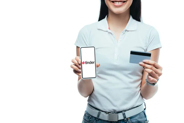 KYIV, UKRAINE - JULY 15, 2019: cropped view of smiling brunette asian girl holding credit card and smartphone with tinder app isolated on white — Stock Photo