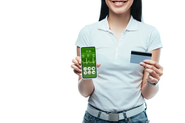 Cropped view of smiling brunette asian girl holding credit card and smartphone with healthcare app isolated on white — Stock Photo