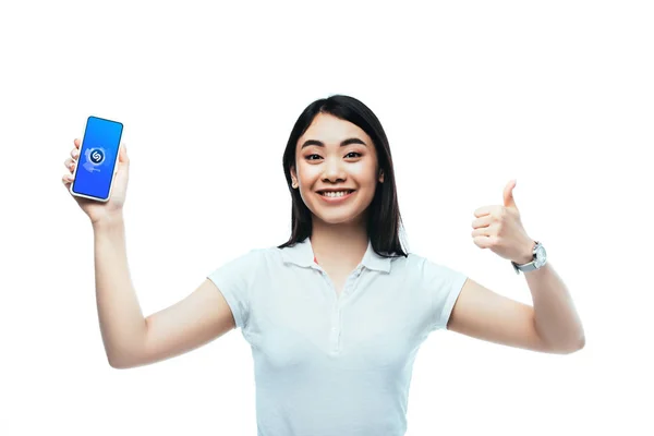 KYIV, UKRAINE - JULHO 15, 2019: feliz morena asiática mulher segurando smartphone com aplicativo shazam e mostrando polegar para cima sinal isolado no branco — Fotografia de Stock
