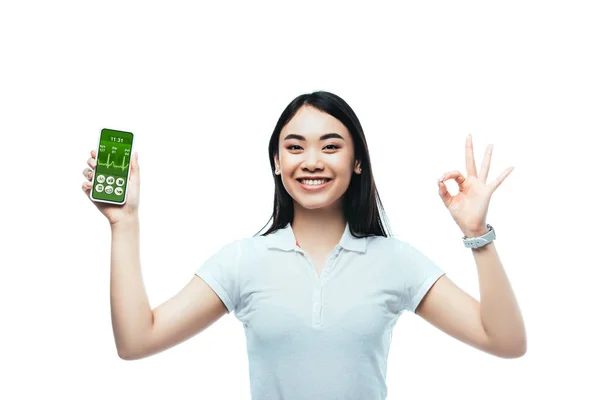 Feliz morena asiático mulher segurando smartphone com saúde app e mostrando ok sinal isolado no branco — Fotografia de Stock