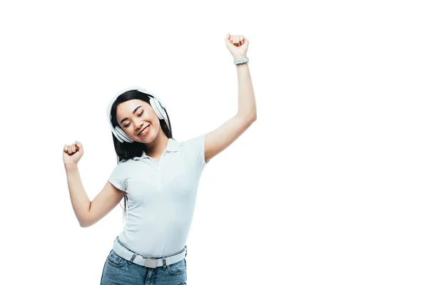 Усміхнена приваблива азіатська дівчина танцює в навушниках ізольована на білому — стокове фото