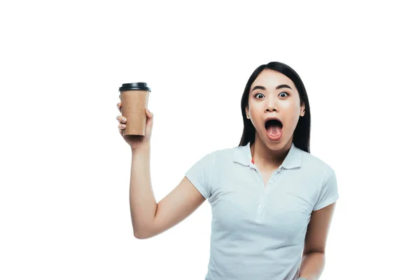 Шокована приваблива азіатська дівчина з відкритим ротом тримає паперову чашку ізольовано на білому — стокове фото
