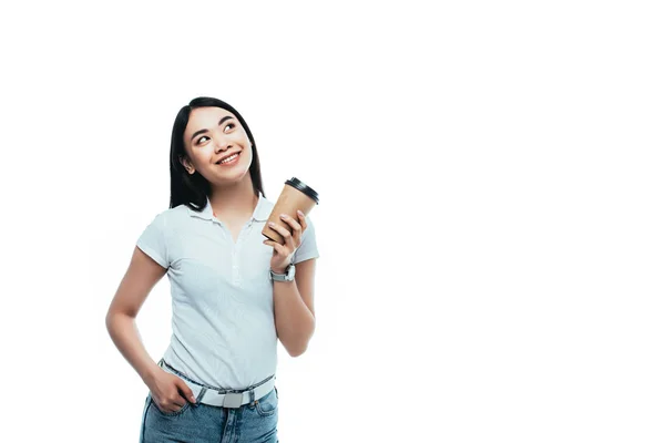 Усміхнена приваблива азіатська дівчина тримає паперову чашку і дивиться ізольовано на білому — стокове фото