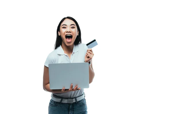 Aufgeregt attraktive asiatische Mädchen mit offenem Mund halten Kreditkarte und Laptop isoliert auf weiß — Stockfoto