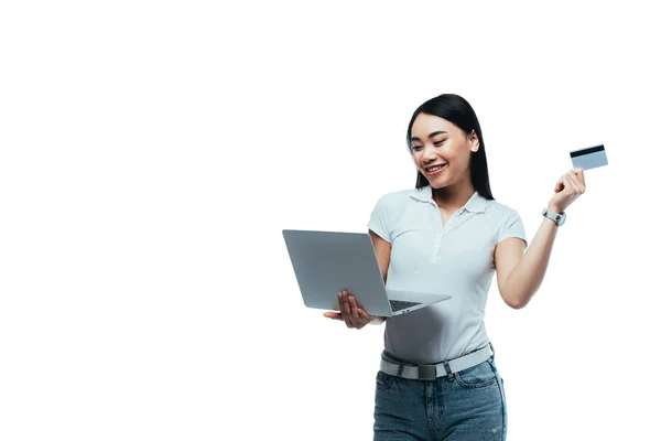 Счастливая привлекательная азиатская девушка держит кредитную карту и ноутбук изолирован на белом — стоковое фото
