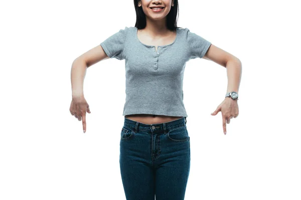 Abgeschnittene Ansicht eines lächelnden attraktiven asiatischen Mädchens, das mit den Fingern nach unten zeigt, isoliert auf weißem Grund — Stockfoto