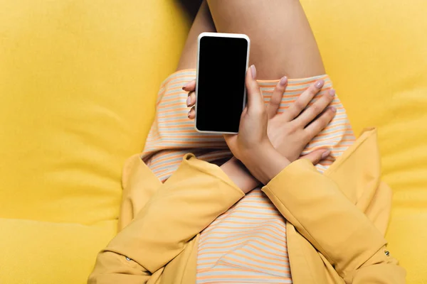 Вид зверху бізнес-леді, що сидить на жовтому дивані і тримає смартфон з порожнім екраном — стокове фото