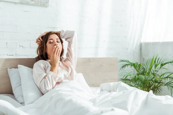 Attraktive Frau im Pyjama mit geschlossenen Augen, die am Morgen gähnt — Stockfoto