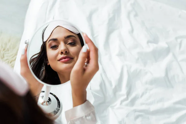 Reflection of attractive woman with sleeping mask looking at mirror at morning — Stock Photo