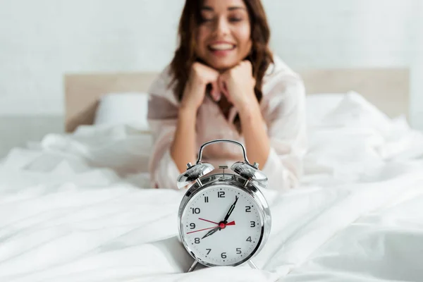 Selective focus of attractive woman looking at alarm clock at morning — Stock Photo