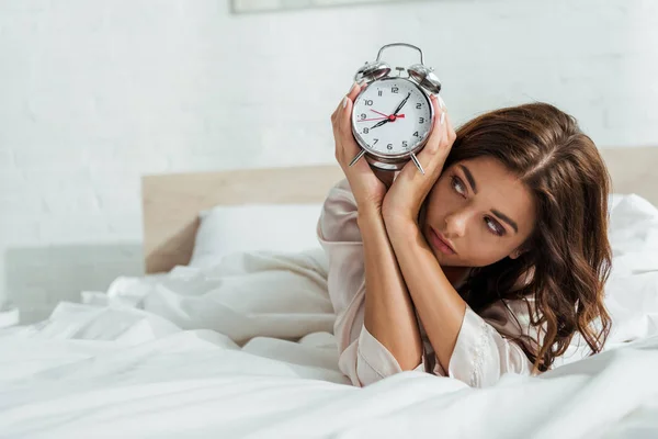 Attraktive Frau hält Wecker und liegt morgens im Bett — Stockfoto