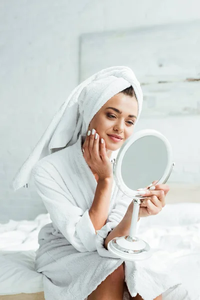 Mujer atractiva en albornoz y toalla mirando el espejo por la mañana - foto de stock