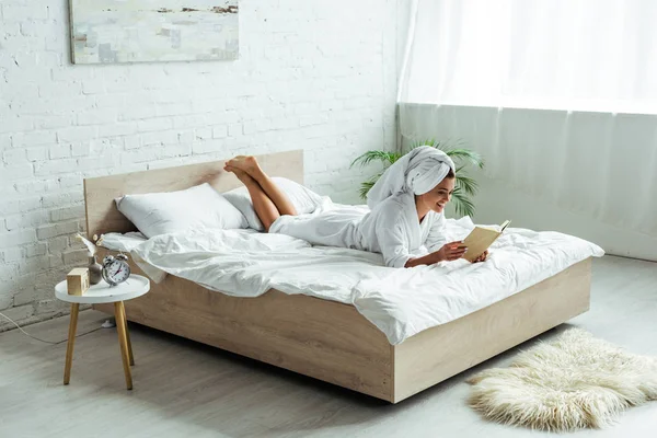 Attraente donna in asciugamano e accappatoio lettura libro al mattino — Foto stock