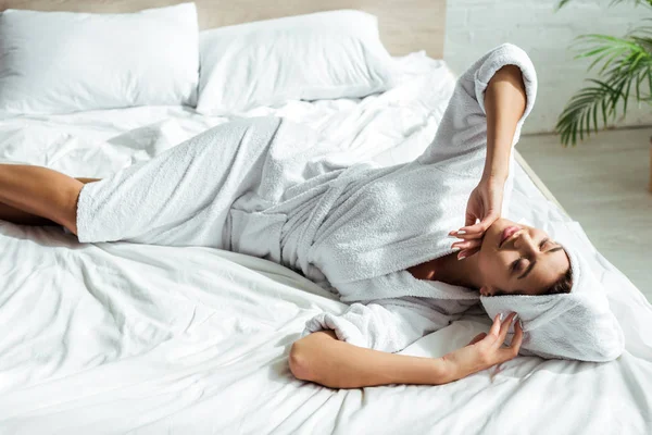 Mulher atraente em roupão de banho e toalha deitada na cama de manhã — Fotografia de Stock