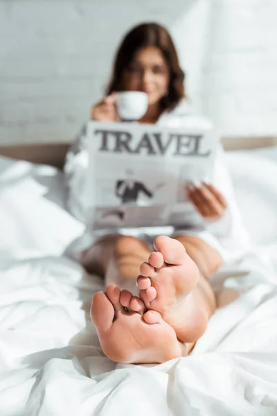 Messa a fuoco selettiva della donna attraente in camicia bianca bere caffè e leggere il viaggio giornale al mattino — Foto stock