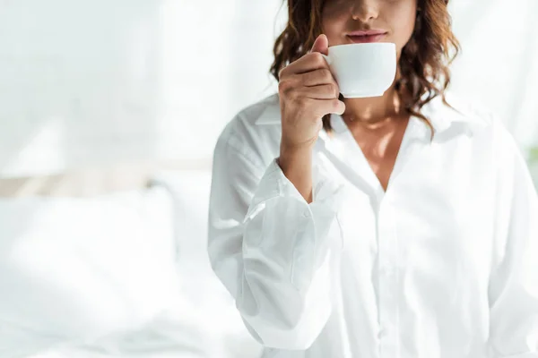 Vista ritagliata della donna in camicia bianca che tiene la tazza al mattino — Foto stock