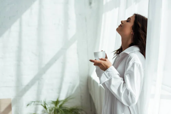 Seitenansicht einer attraktiven Frau im weißen Hemd, die morgens eine Tasse hält — Stockfoto