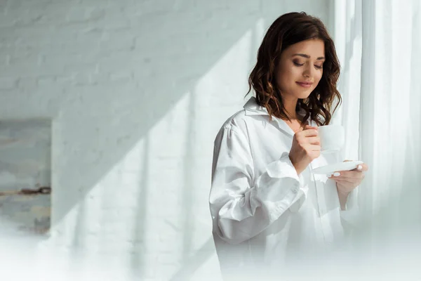 Jolie femme en chemise blanche tenant tasse le matin — Photo de stock