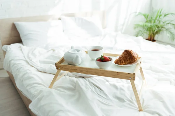 Bandeja de madera con tetera, arriba, croissant y fresas por la mañana - foto de stock