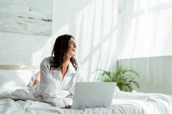 Улыбающаяся и привлекательная женщина с ноутбуком смотрит в сторону утром — стоковое фото