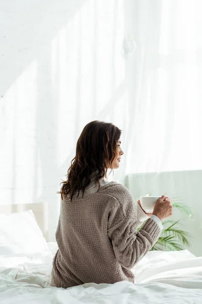 Back view of woman in grey sweater holding cup of tea at morning — Stock Photo