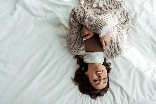 Vista dall'alto della donna sorridente in maglione sdraiata a letto al mattino — Foto stock