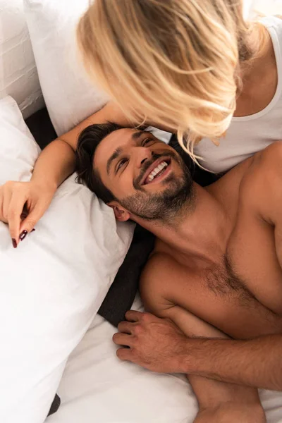 Mulher loira abraçando seu namorado sorridente na cama pela manhã — Fotografia de Stock