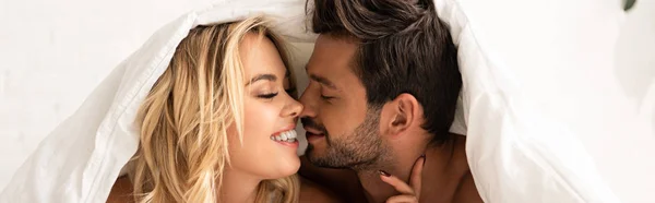 Glückliches zartes Paar, das sich morgens unter Bettlaken küsst — Stockfoto