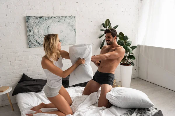 Feliz joven pareja teniendo divertido y almohada batalla en la cama - foto de stock