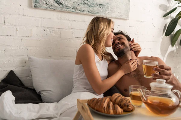 Couple heureux embrasser et prendre le petit déjeuner au lit le matin — Photo de stock