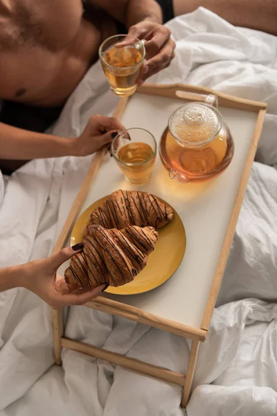 Vista ritagliata di coppia che prende tè e croissant per la colazione a letto al mattino — Foto stock