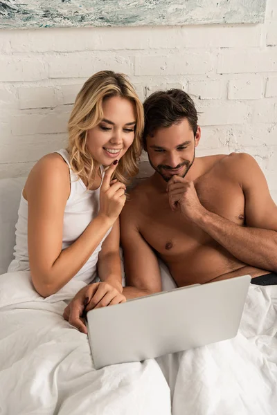 Sonriente pareja usando portátil en la cama por la mañana - foto de stock