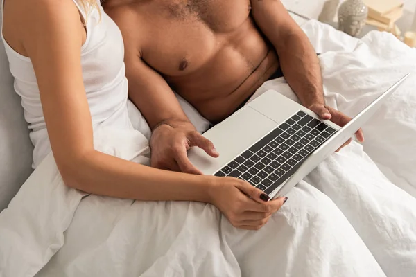 Vista recortada de la pareja usando el ordenador portátil en la cama por la mañana - foto de stock