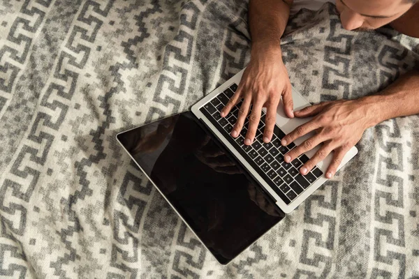 Верхний вид человека, лежащего на кровати и с помощью ноутбука с пустым экраном — стоковое фото