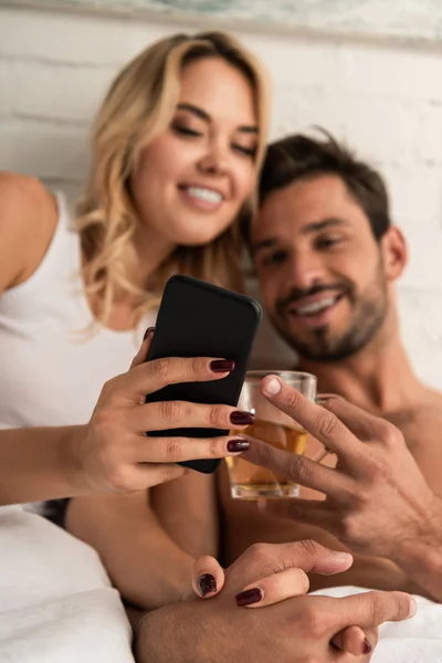 Foco seletivo de casal feliz com chá usando smartphone na cama pela manhã — Fotografia de Stock