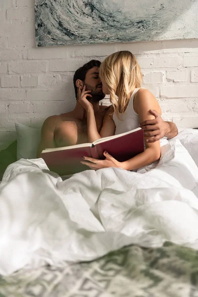 Bella coppia tenera baciare e tenere libro a letto al mattino — Foto stock