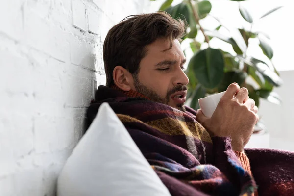 Sick man with cup of hot drink lying in bed at home — Stock Photo