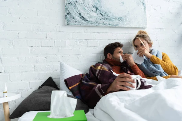 Casal doente com narizes escorrendo deitado na cama com guardanapos — Fotografia de Stock