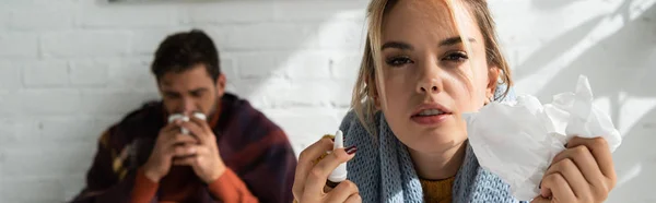 Mujer enferma sosteniendo aerosol nasal y servilletas en el dormitorio con el hombre detrás — Stock Photo
