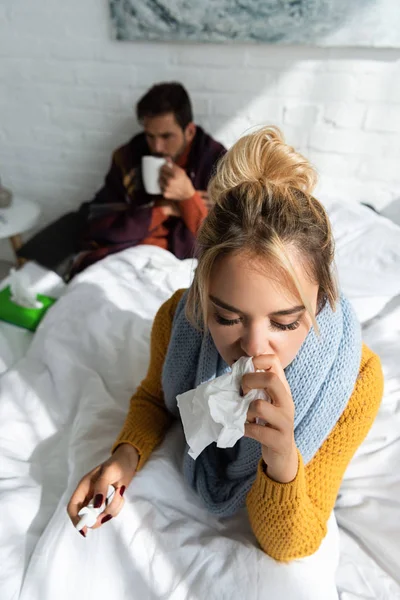 Malade femme tenant pulvérisation nasale et serviettes dans la chambre avec l'homme derrière — Photo de stock
